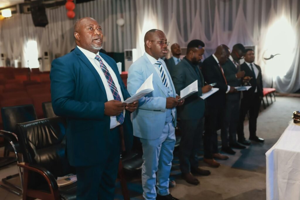A group of men in suits holding papers during a formal indoor ceremony.